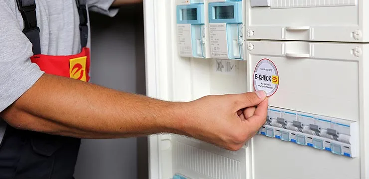 Elektrofachmann bringt E-Check Plakette an